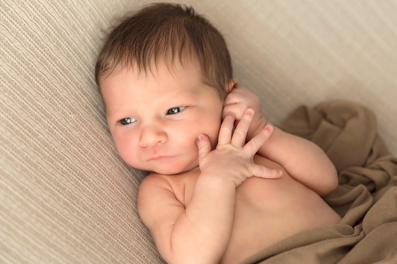 newbornshooting neugeborenenshooting babyshooting GeistFrei Ein ruhendes Baby mit kurzem Haar, das auf einer Decke liegt und neugierig schaut.