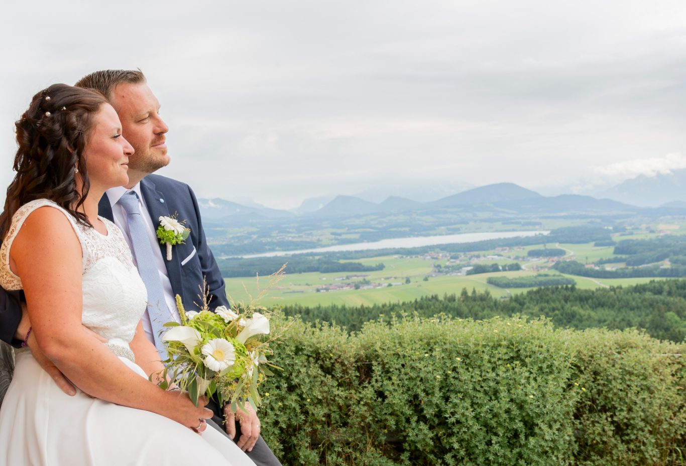 hochzeitsfotografie GeistFrei! Brautpaar posiert mit Blick auf eine grüne Landschaft und Berge im Hintergrund.