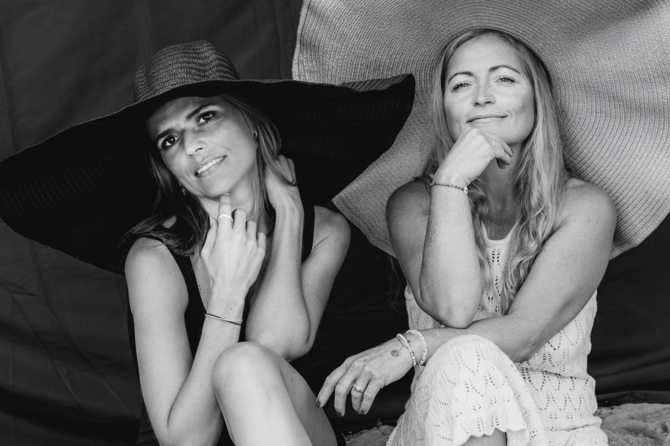 Zwei Frauen in Schwarz-Weiß, eine mit großem Hut Zwei Frauen in Schwarz-Weiß, eine mit großem Hut, beide lächelnd und nachdenklich.