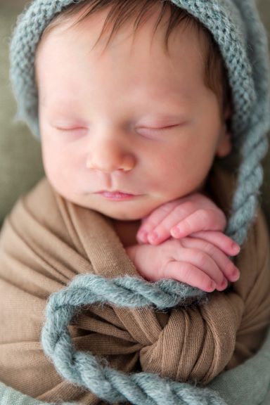 Neugeborenes Baby, sanft in ein braunes Tuch gewickelt, mit einer blauen Mütze.