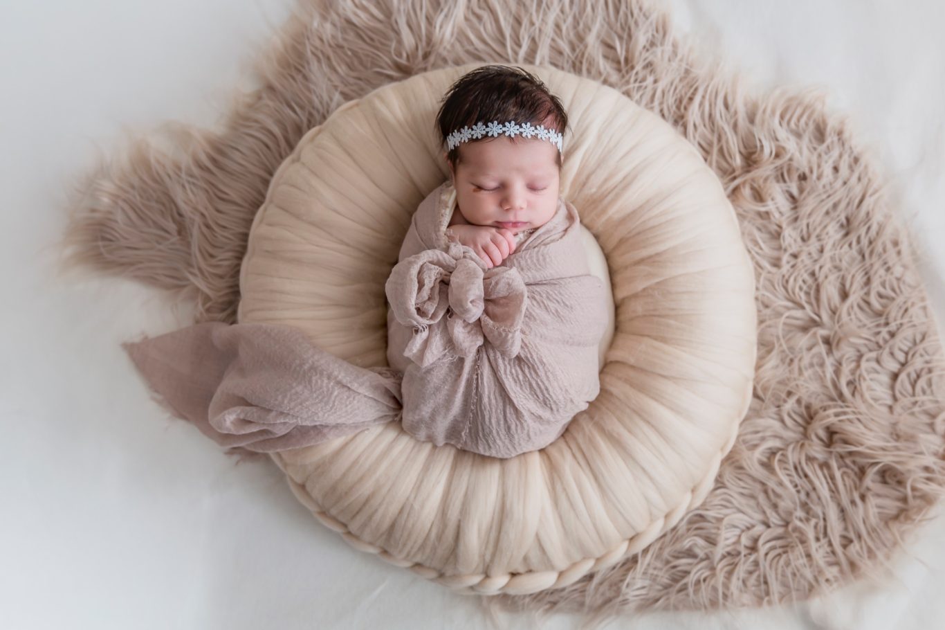 newbornshooting neugeborenenshooting babyshooting GeistFrei Ein schlafendes Baby in einer beigen Decke, umgeben von einem weichen, runden Kissen.