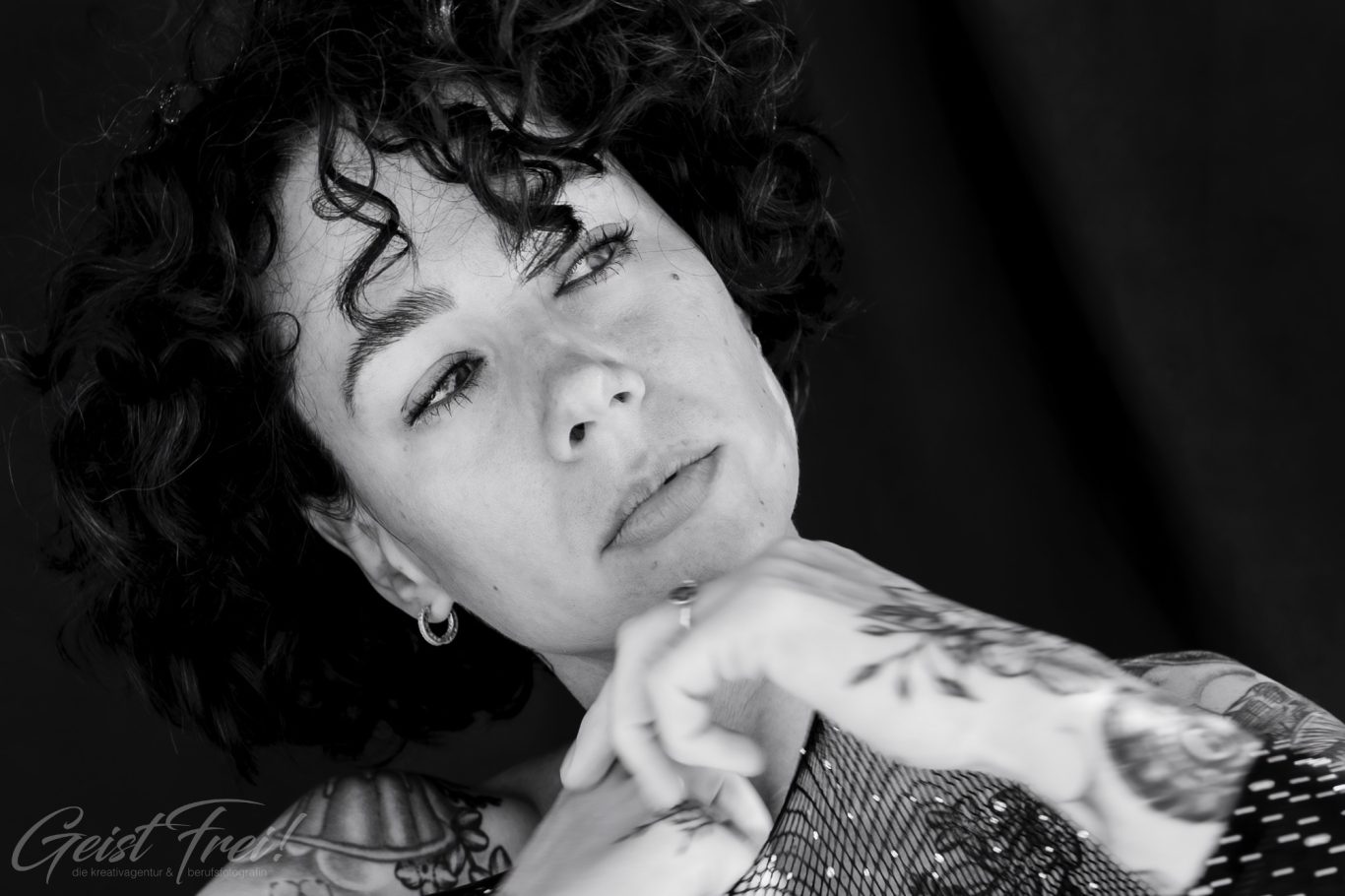 Schwarz-weiss Porträt einer Frau Porträt einer nachdenklichen Frau mit lockigem Haar und sichtbaren Tattoos.