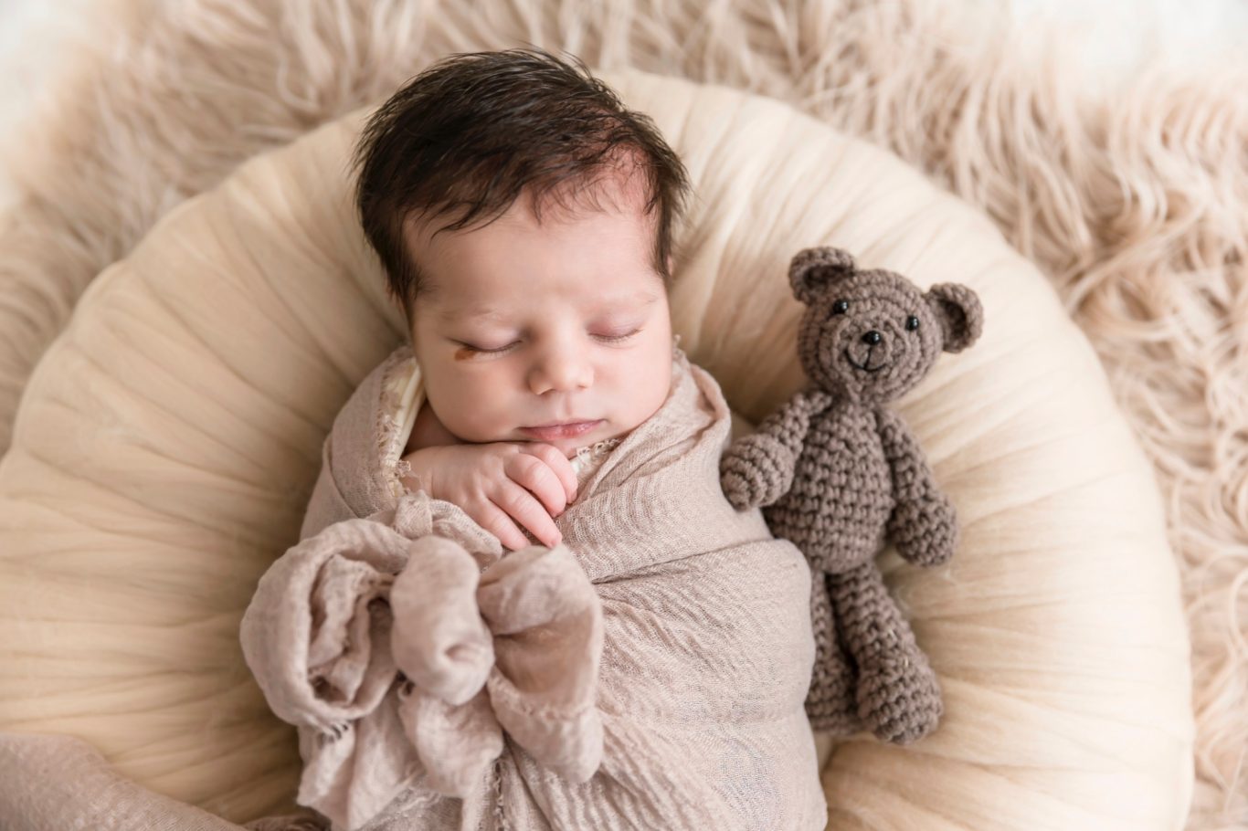 newbornshooting babyshooting GeistFrei Ein schlafendes Baby in einer beigen Decke, neben einem gehäkelten Teddy.
