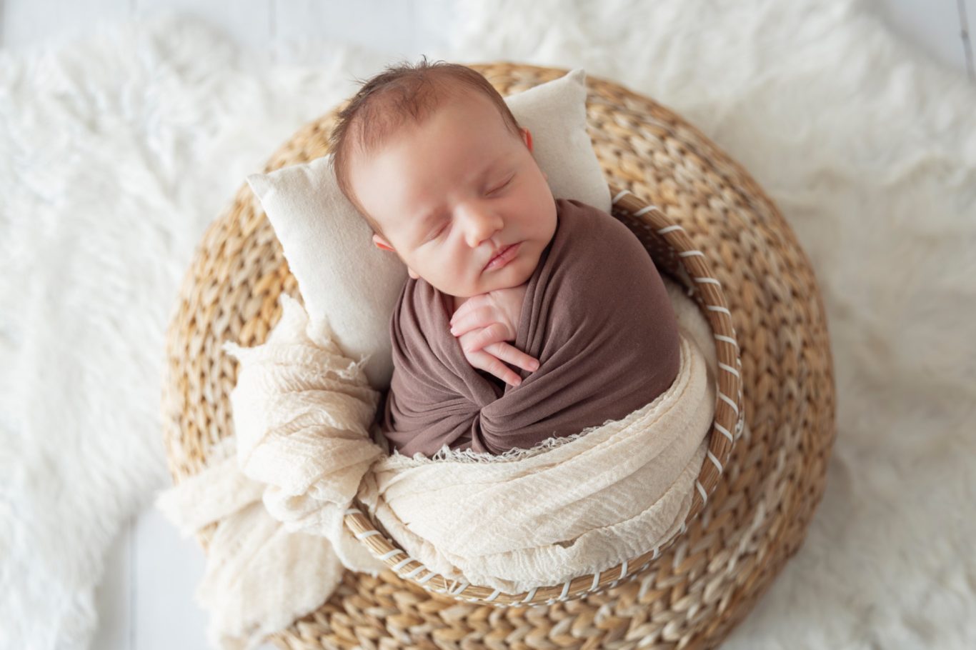 babyshooting GeistFrei! Neugeborenes Baby, sanft eingewickelt in Tücher, liegt auf einem geflochtenen Korb.