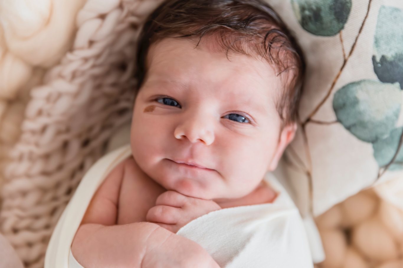 newbornshooting babyshooting familienfotografie GeistFrei Ein Neugeborenes mit blauen Augen, das auf einem Kissen mit Blättermuster liegt.