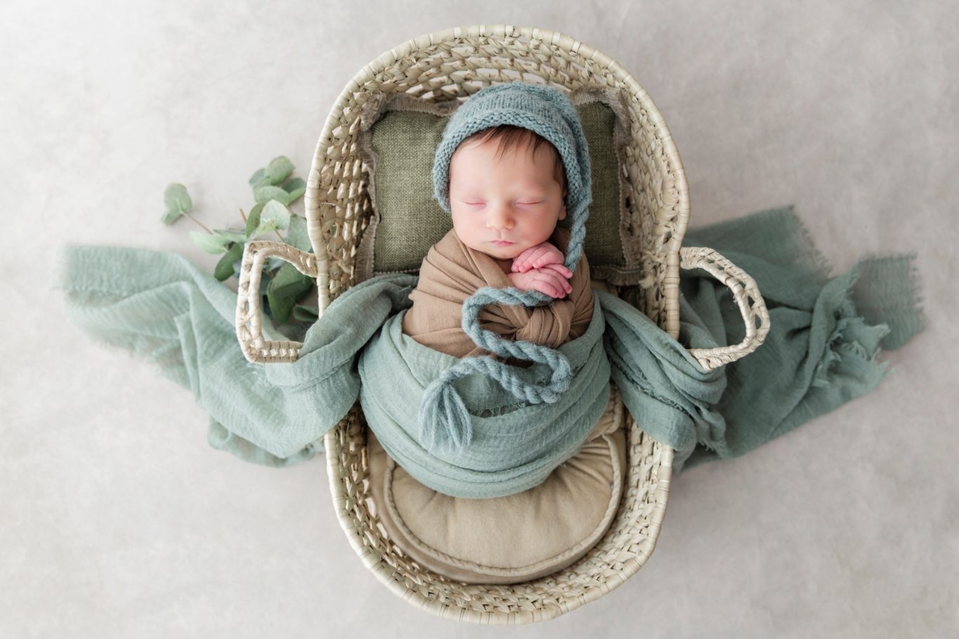 newbornshooting neugeborenenshooting babyshooting GeistFrei Ein schlafendes Neugeborenes in einer Körbchen mit blauen Tüchern und sanften Farben.