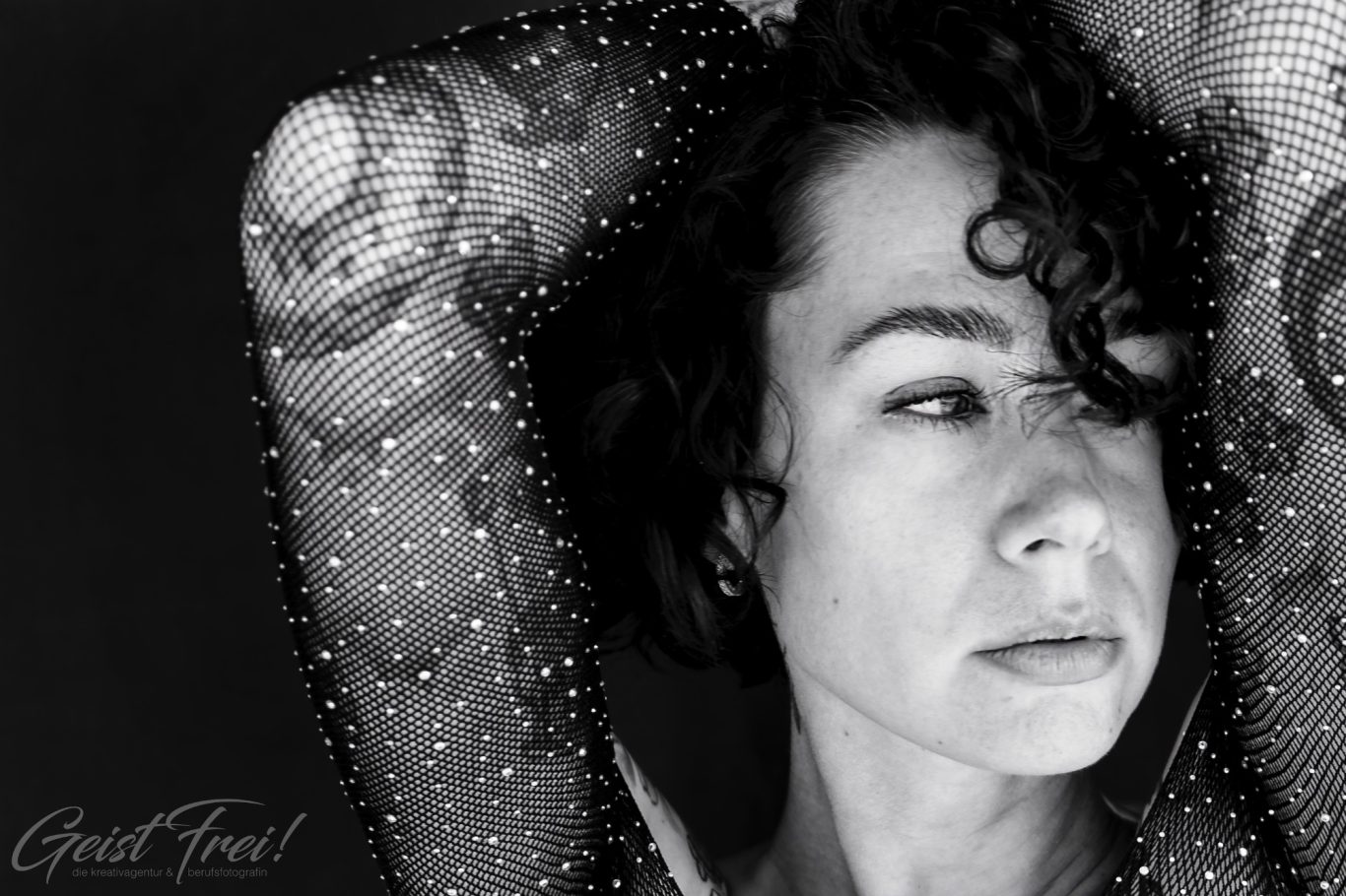 Schwarz-weiss Porträt einer Frau Porträt einer Frau mit Locken und Tattoos, ausdrucksvoller Blick auf dunklem Hintergrund.