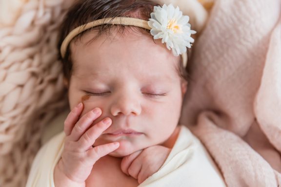 Neugeborenes Baby mit Blume, liegt entspannt auf einem weichen Tuch.
