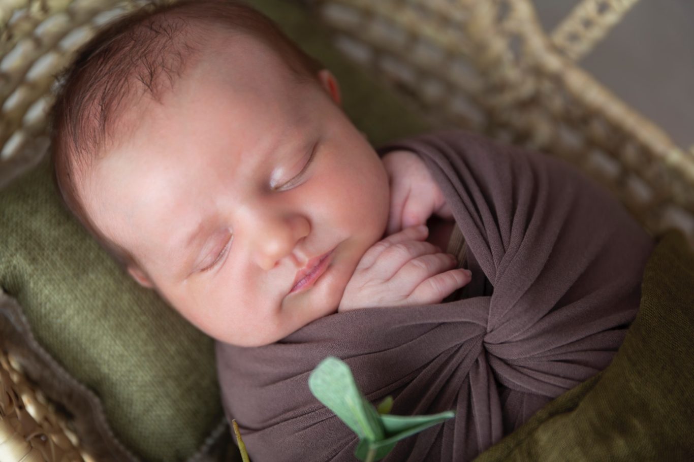neugeborenenfotografie GeistFrei! Schlafendes Neugeborenes in brauner Decke, sanft eingerollt und mit Händen zusammen.