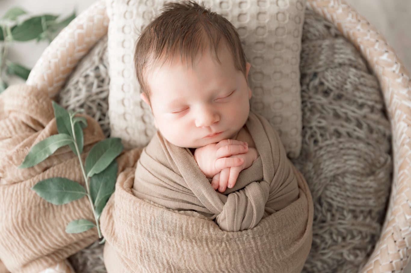 newbornshooting neugeborenenshooting babyshooting GeistFrei Neugeborenes Baby, sanft eingewickelt in einem beige Tuch, schläft in einem Korb.