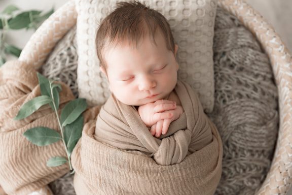 Schlafendes Baby, sanft in ein braunes Tuch gewickelt, in einem Korb auf einem Kissen.