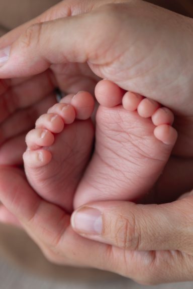 Ein Babyfuß liegt in einer Hand von Erwachsenen, umgeben von weiteren Händen.