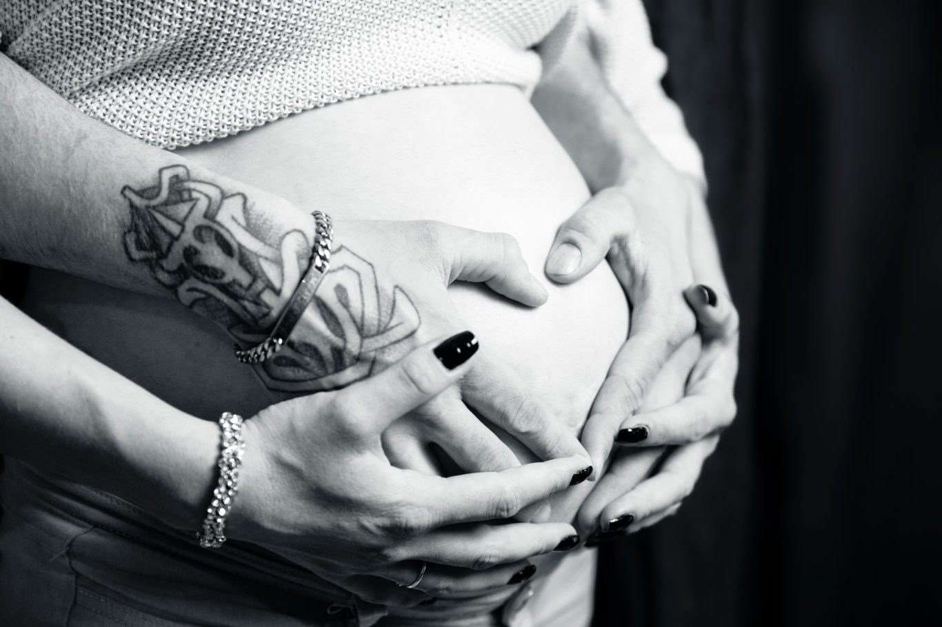 babybauchshooting babybauchfotografie werdende Mama GeistFrei Hände um einen schwangeren Bauch mit Tätowierungen und schwarzen Nägeln.