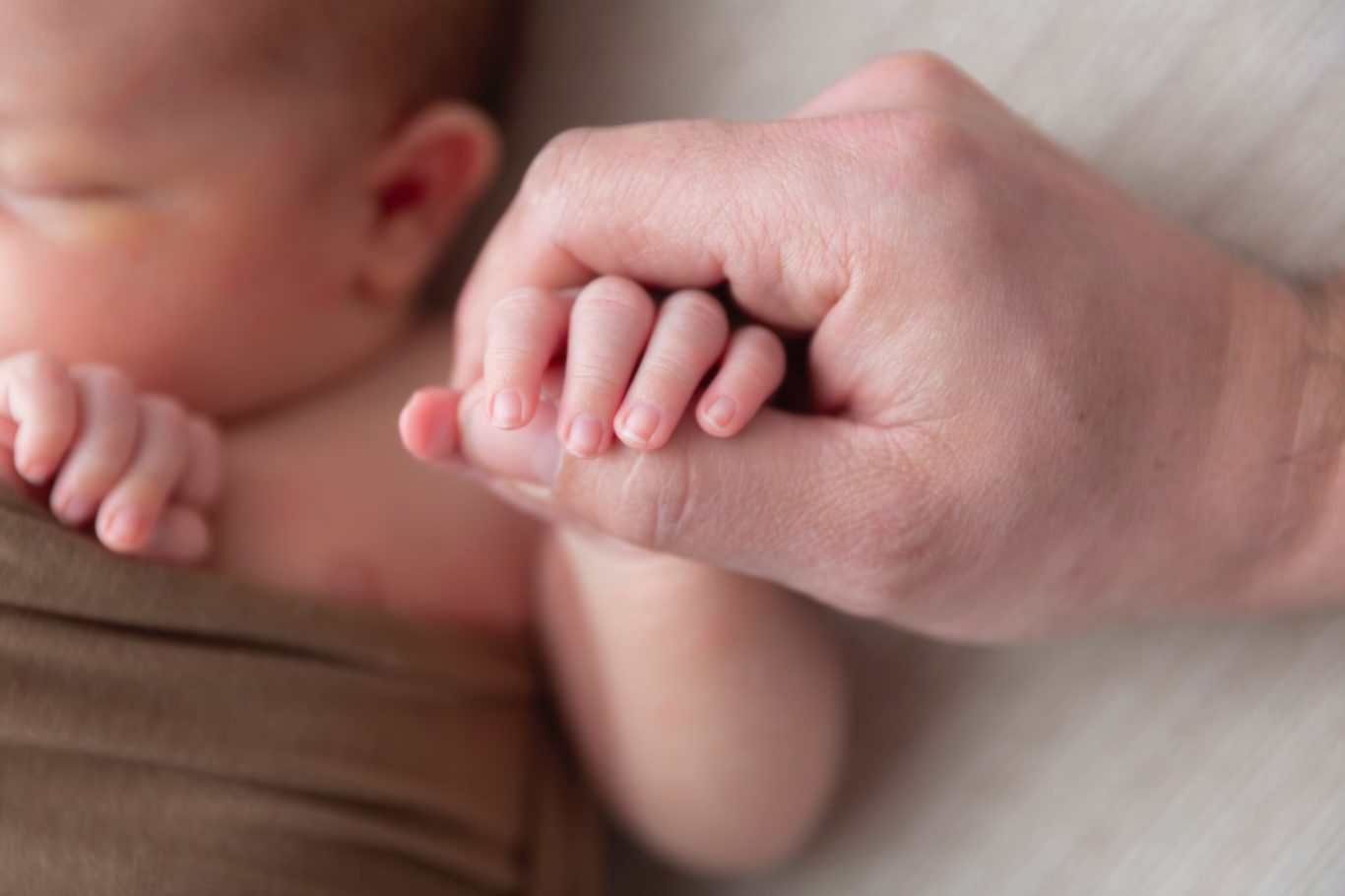 Verbundenheit - newborn GeistFrei! Eine Hand hält sanft die kleine Hand eines Neugeborenen.