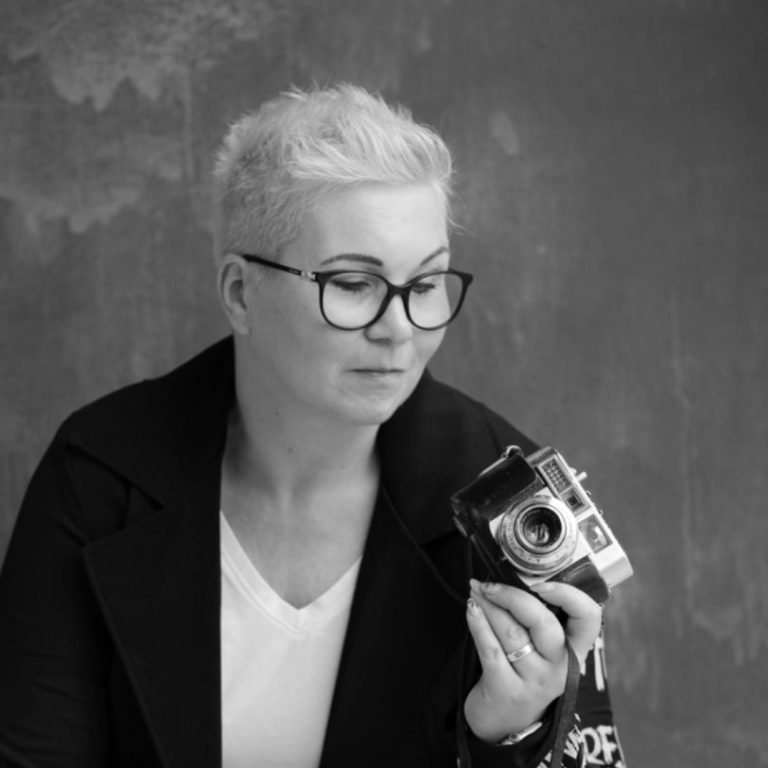 business brand fotografie porträt GeistFrei! Frau mit kurzen blonden Haaren und Brille hält eine Kamera in der Hand.