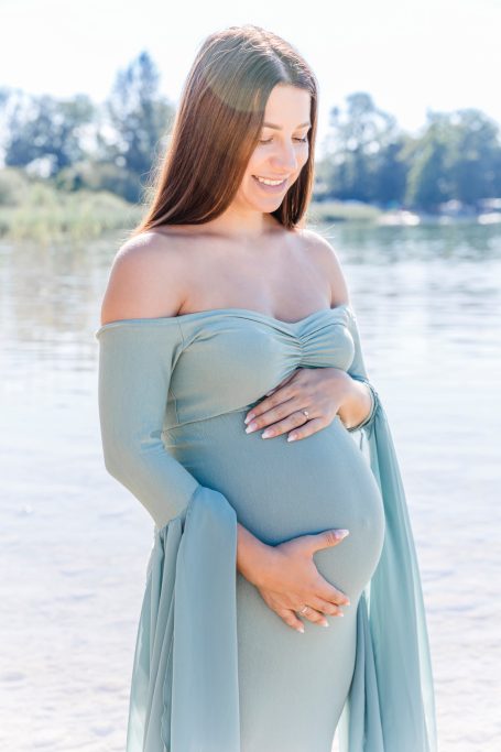 Schwangere Frau in einem fließenden, mintgrünen Kleid am Wasser.