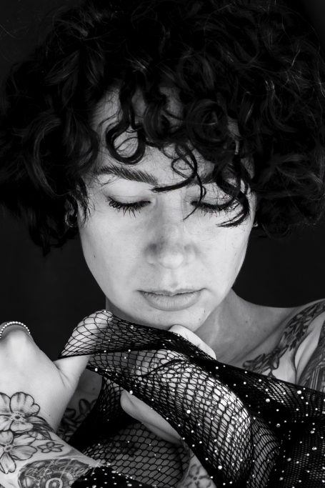 Frau mit lockigem Haar, die nachdenklich mit einem Schal spielt.