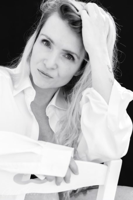 Porträt einer Frau mit blonden Haaren, die nachdenklich aussieht und einen weißen Hemd trägt.