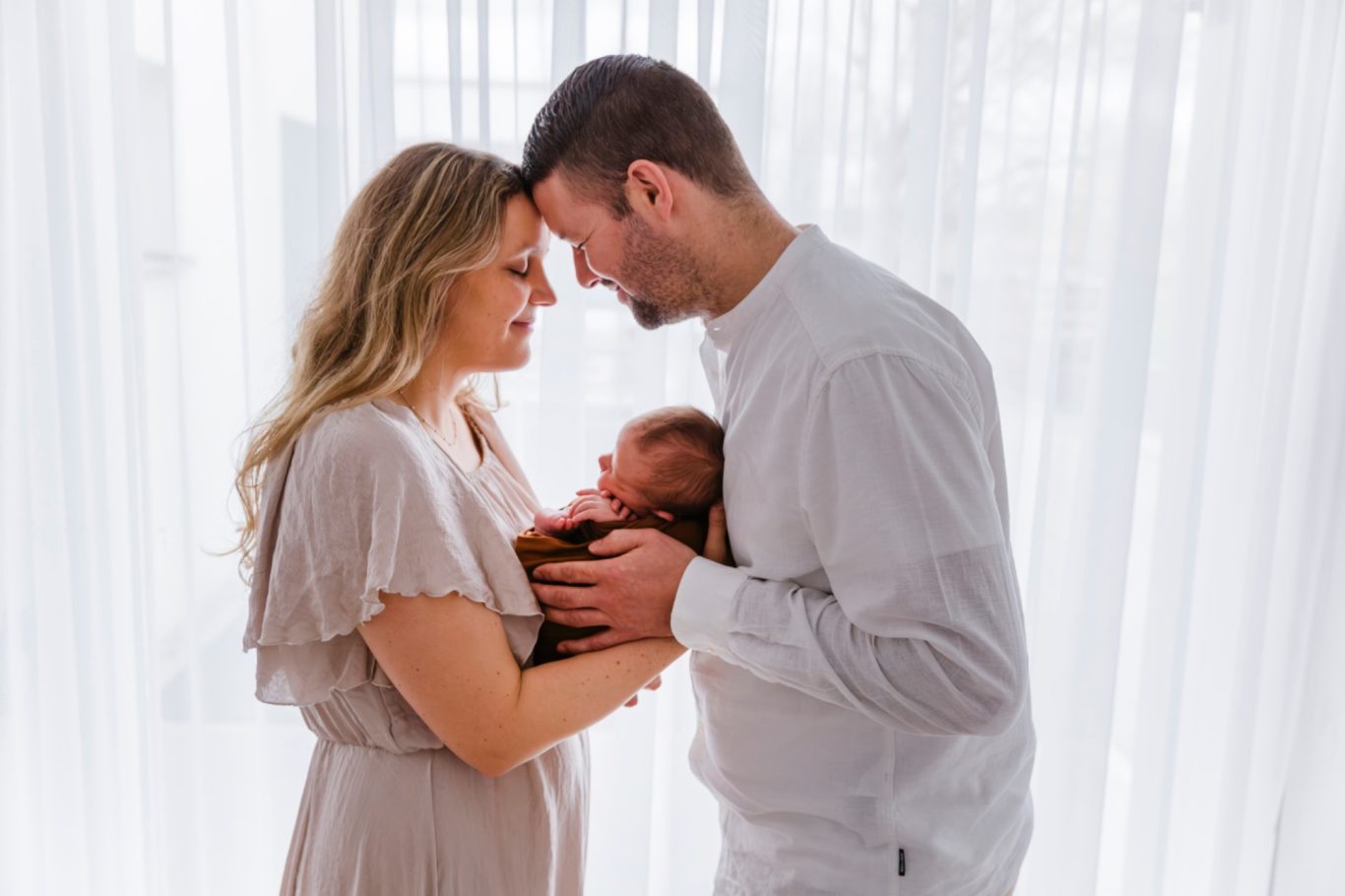 famileienfotografie glückliche Eltern GeistFrei! Ein Paar hält ein Neugeborenes in den Händen, umgeben von hellem Licht.